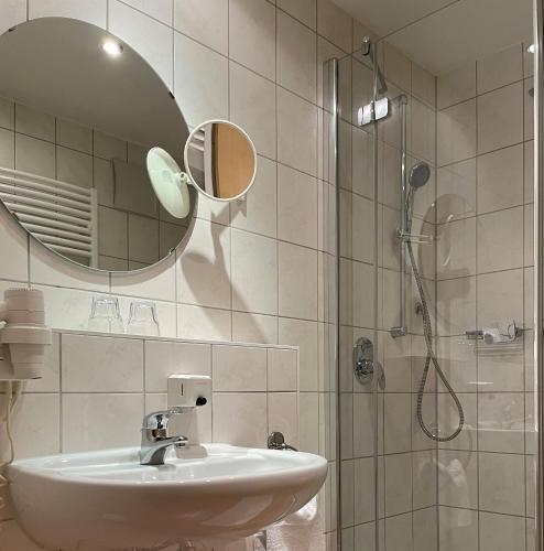 a bathroom with a sink and a shower with a mirror at Hotel Bettina garni in Günzburg