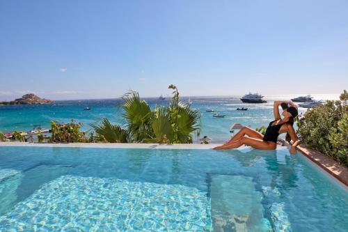 two women sitting in a swimming pool next to the ocean at Mykonos Dove Beachfront Hotel in Platis Yialos Mykonos