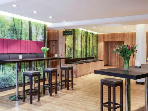 a bar with stools in a room with trees at Mercure Hotel am Messeplatz Offenburg in Offenburg