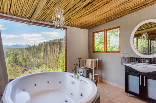a bathroom with a tub and a sink and a large window at Forest Valley Cottages in Knysna