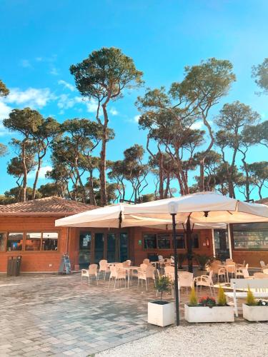 a restaurant with white tables and chairs and trees at ISOLA VERDE Camping Village in Nettuno