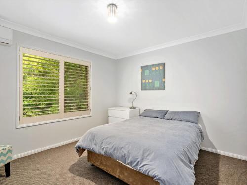 a white bedroom with a bed and a window at Spacious House with Balcony & Pool, Walks to Beach in Terrigal