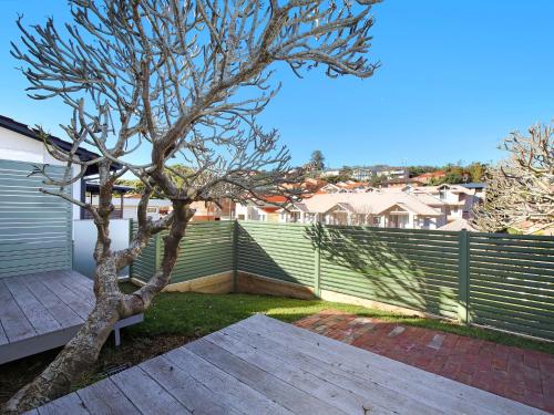 a tree sitting next to a wooden bench next to a fence at Cosy Studio With Deck, Close to Shops and Beach in Terrigal