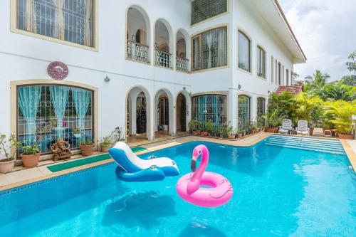 a swimming pool in front of a house with two inflatable flamingos at Casa Do Amor by VEO - Part of StayVista in Sangolda
