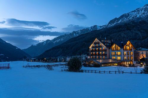 a large building in a snowy field with mountains at Hotel Sant'Orso - Mountain Lodge & Spa in Cogne