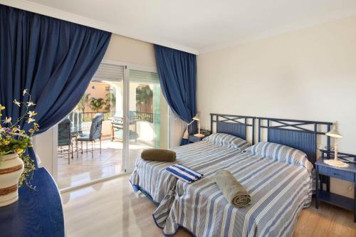 1 dormitorio con 1 cama con cortinas azules y balcón en Hacienda Playa Elviria Marbella, en Marbella