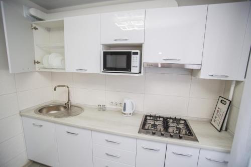 eine weiße Küche mit einer Spüle und einer Mikrowelle in der Unterkunft Bilius Apartment in Winnyzja