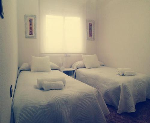 um quarto com 2 camas com lençóis brancos e uma janela em Apartamento adosado cerca del mar em Gran Alacant