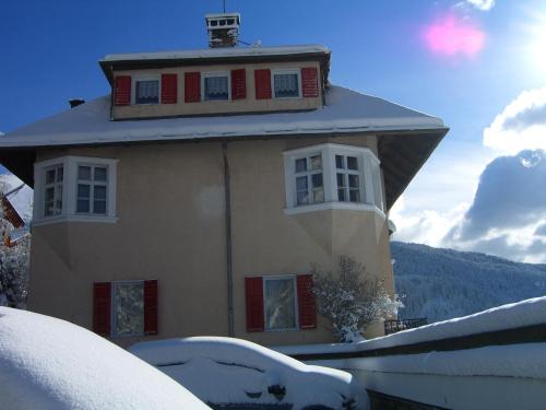 a house with red shuttered windows in the snow at Hotel Villa Emilia in Ortisei