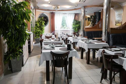 un restaurant avec des tables blanches, des chaises et des plantes dans l'établissement Park UNESCO Residence, à Łęknica