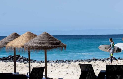 a person walking on the beach with a surfboard at Agua Hotels Sal Vila Verde in Santa Maria