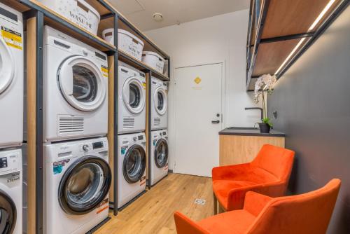 a laundry room with four washing machines and an orange chair at Cosy Duo Loft - self check-in in Tartu