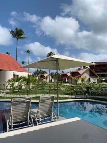 zwei Stühle und ein Sonnenschirm neben einem Pool in der Unterkunft Oka Muro Alto in Porto De Galinhas