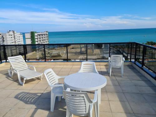 een witte tafel en stoelen op een balkon met uitzicht op de oceaan bij Apartamento Catamarã Port Ville Pajuçara Maceió in Maceió