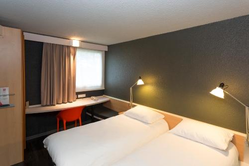 a hotel room with two beds and a desk and a window at ibis Lorient Centre Hôtelier in Caudan