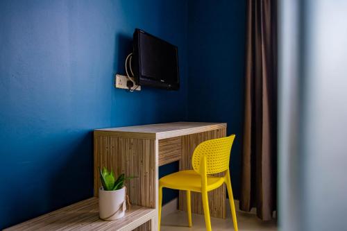 einen Schreibtisch mit einem gelben Stuhl und einen TV an einer blauen Wand in der Unterkunft BEEZ Hotel Kuala Lumpur in Kuala Lumpur