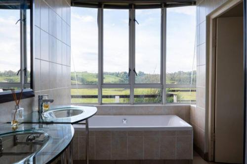 baño con 2 lavabos y bañera con ventana en Highlands Farm House, en Van Reenen