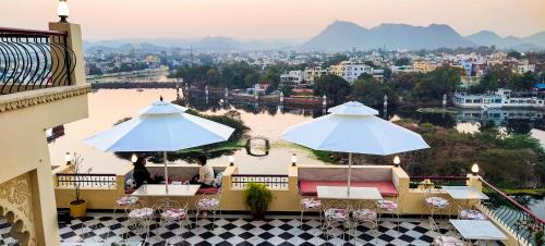 two people sitting under umbrellas on a balcony overlooking a river at Hotel Mewari Villa in Udaipur