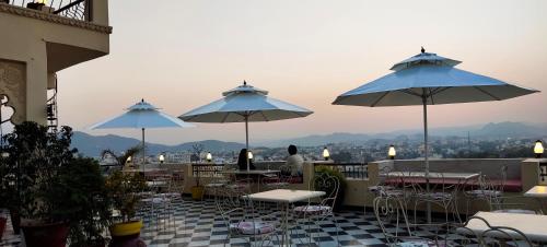 a patio with tables and chairs and umbrellas at Hotel Mewari Villa PURE VEG in Udaipur