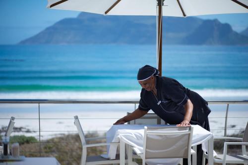 a man bending over a table in front of the ocean at Last Word Long Beach in Kommetjie