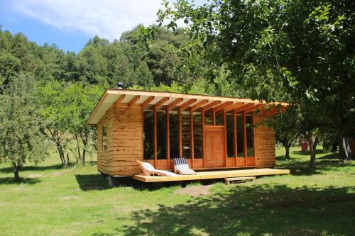 a small wooden cabin with two chairs in a field at Karkú Lodge in Pucón
