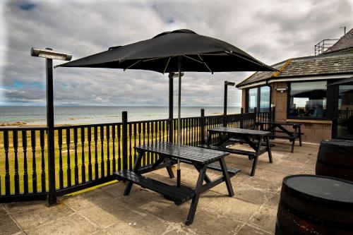 two picnic tables and an umbrella on the beach at GOLF View Hotel & Macintosh Restaurant in Lossiemouth