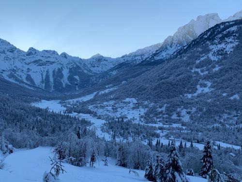 a view of a snowy mountain valley with trees and a river at Bujtina Malaj in Valbonë