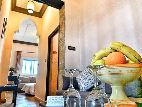 a bowl of fruit on a table with two wine glasses at Riad Al Madina in Essaouira