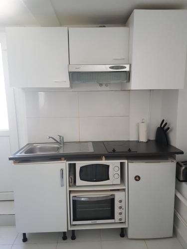 a white kitchen with a microwave and a sink at Studio neuf meublé Rosny-sous-Bois in Rosny-sous-Bois