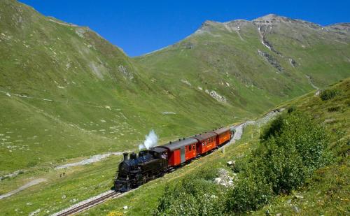 a train traveling down the tracks in the mountains at Hotel Tenne in Reckingen - Gluringen