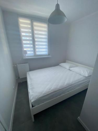 ein weißes Bett in einem Zimmer mit Fenster in der Unterkunft APARTAMENT OŚ. JASNE 19B in Dzierżoniów