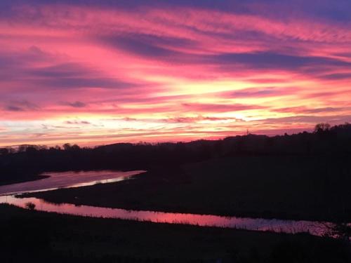 a sunset over a river in a field at Lough Erne Glamping Pod in Enniskillen