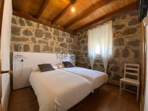 1 dormitorio con 1 cama grande en una pared de piedra en Casa Serapio, en Ávila