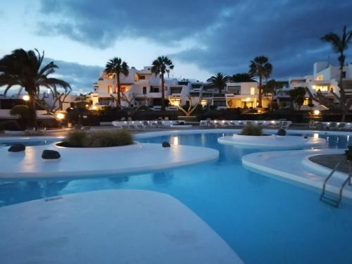 una piscina notturna con edifici sullo sfondo di El Gueco Holiday Apartment a Costa Teguise