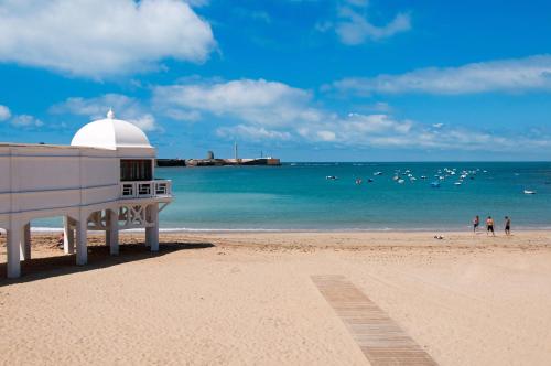 a building on a beach with people in the water at Occidental Cádiz in Cádiz