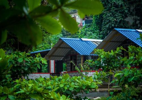 a house with blue roofs in the trees at STAYMAKER River Wood Residency in Dandeli