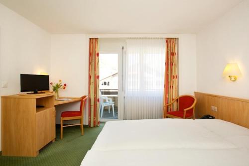 Habitación de hotel con cama, escritorio y TV. en Gornergrat Dorf Hotel, en Zermatt