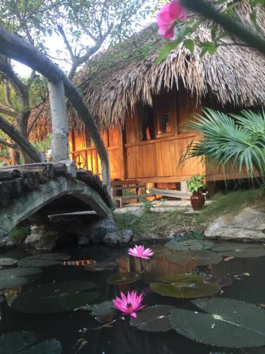 a pond with pink flowers in front of a hut at Hang Lan Bungalow in Ninh Binh