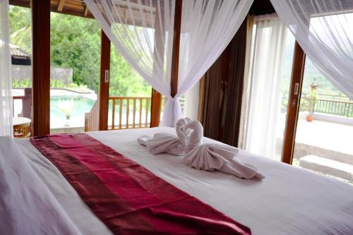 een slaapkamer met een bed met witte lakens en een raam bij Nadya Homestay in Munduk
