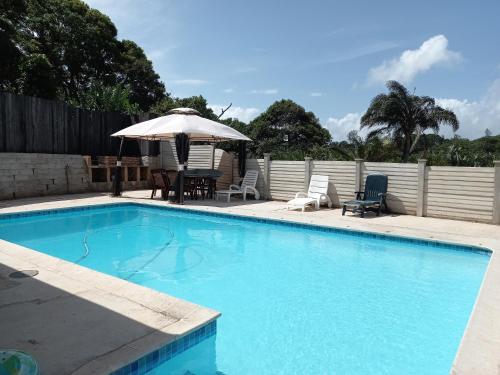 a swimming pool with a table and an umbrella at Poolside Guest House in Port Shepstone