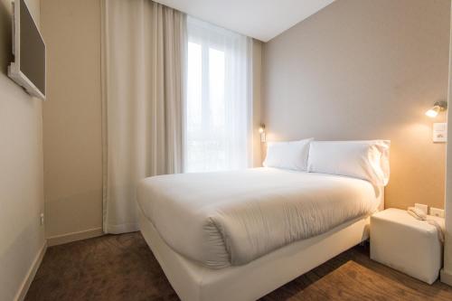 a white bed in a room with a window at Hôtel Ligure in Cannes