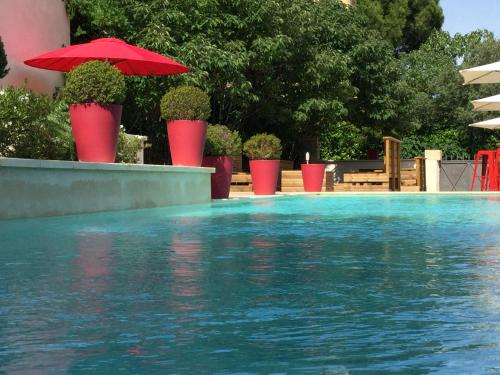 a swimming pool with red umbrellas and a swimming pool at Boutique Hôtel La Villa MONTESQUIEU in Laudun