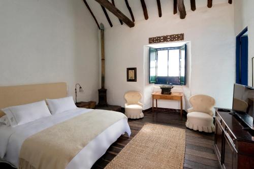 a bedroom with a bed and two chairs and a television at Casa La Bisbal in Cucunubá