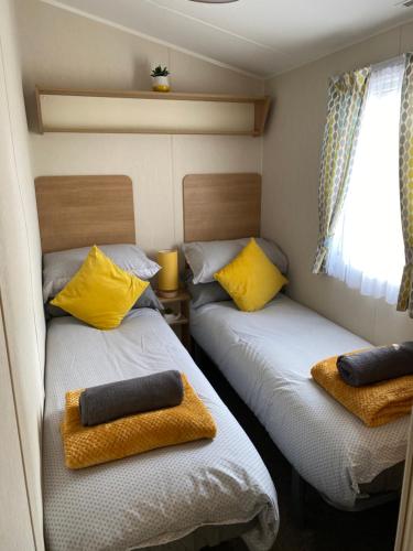 Duas camas num pequeno quarto com almofadas amarelas em Dixons den em Swarland