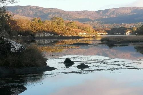 a river with rocks in the water with mountains in the background at Harbourside House Glengarriff in Glengarriff