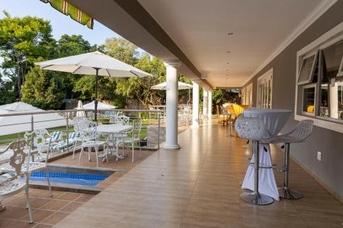 a porch with chairs and tables and an umbrella at Dikalo Highston Boutique Guest house in Bryanston Sandton Johannesburg in Johannesburg