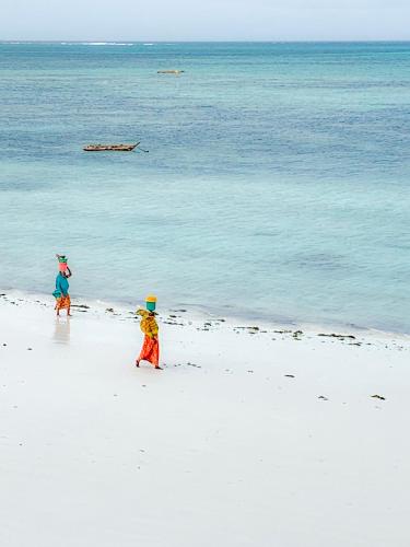 two people walking on a beach near the water at The African Paradise Beach Hotel in Bwejuu
