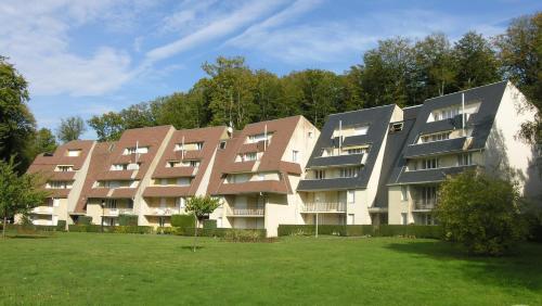 un gran edificio de apartamentos con un campo verde delante de él en appartement au Hameau du parc des thermes, en Bagnoles de l'Orne