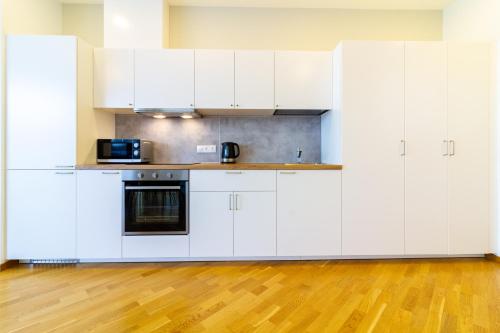 a kitchen with white cabinets and a wooden floor at Elija Swan-Toy Apartments in Šventoji