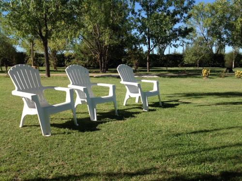 three white chairs sitting in the grass in a park at Establecimiento Rural El Chañar in San Rafael